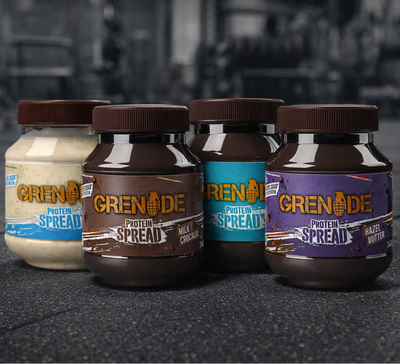 Four bottles of Grenade Protein Spread with different flavors on a dark surface.