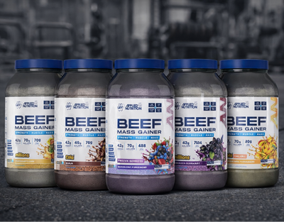 Five bottles of Beef Mass Gainer supplements on a dark surface with a gym background.