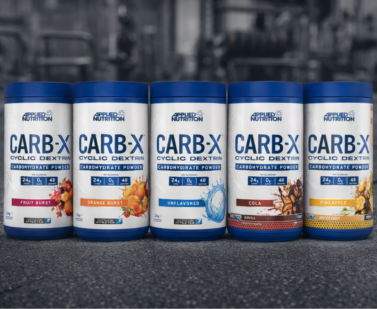 Five containers of Applied Nutrition CARB-X supplement on a dark surface with a blurred gym background.