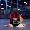 Black container of Animal Cuts supplement with rainbow candy on a gym floor.