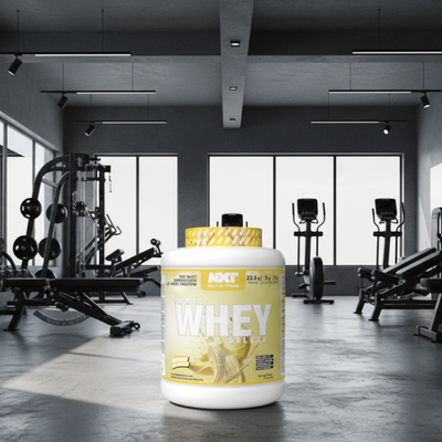 NXT Nutrition Pure Whey Deluxe protein powder container with banana flavour on a gym background