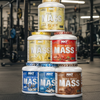 Stack of NXT Pure Whey Mass protein powder containers in various flavors.