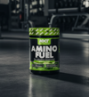 NXT Nutrition Amino Fuel supplement container on a dark surface with gym equipment in the background