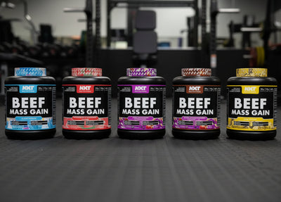Five bottles of beef mass gain supplement on a gym floor.
