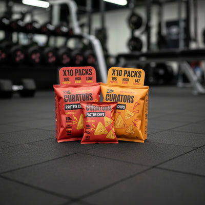 Packages of 'The Curators' protein chips on a gym floor with blurred gym equipment in the background.